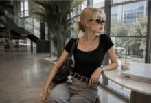 Acubi accessories outfit with black shoulder bag, silver jewelry, sunglasses, belt hardware, fitted black top, grey denim, and modern cafe styling
