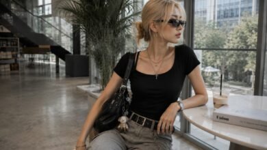 Acubi accessories outfit with black shoulder bag, silver jewelry, sunglasses, belt hardware, fitted black top, grey denim, and modern cafe styling