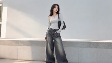 Woman wearing an Acubi aesthetic outfit with fitted grey top, baggy wide-leg jeans, black shoulder bag, silver jewelry, and chunky sneakers