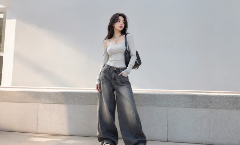 Woman wearing an Acubi aesthetic outfit with fitted grey top, baggy wide-leg jeans, black shoulder bag, silver jewelry, and chunky sneakers