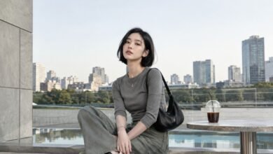 Acubi color palette outfit with grey fitted top, muted green denim, black shoulder bag, black sneakers, silver jewelry, and modern city terrace styling