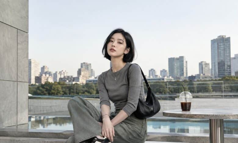 Acubi color palette outfit with grey fitted top, muted green denim, black shoulder bag, black sneakers, silver jewelry, and modern city terrace styling
