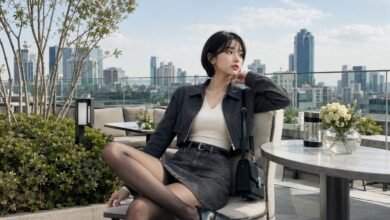Acubi date outfit with black mini skirt, cream fitted top, cropped charcoal jacket, sheer tights, chunky black boots, black shoulder bag, silver jewelry, and rooftop city styling