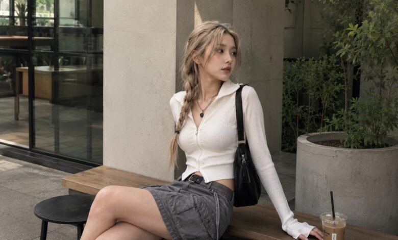 Acubi skirt outfit with white fitted zip top, grey cargo skirt, black shoulder bag, silver jewelry, black belt, and muted café styling