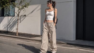 Acubi summer outfit with white cropped tank, loose beige parachute pants, chunky sneakers, black shoulder bag, silver jewelry, and urban cool-girl styling