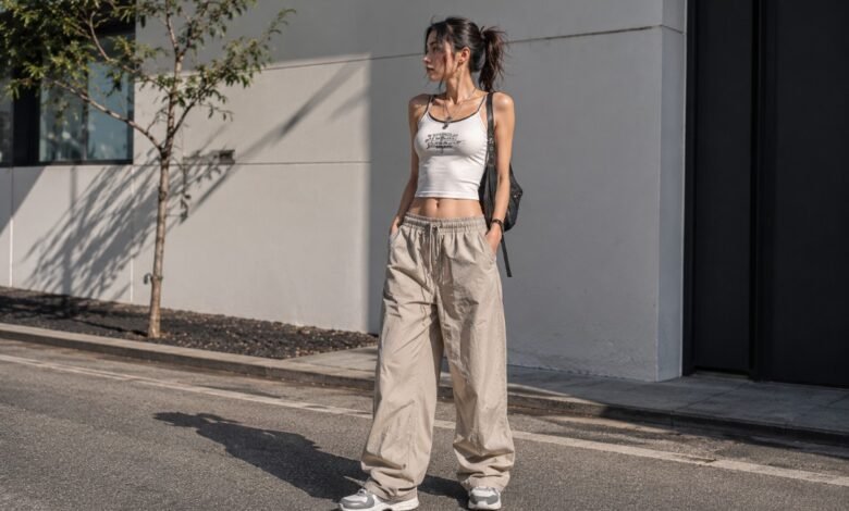 Acubi summer outfit with white cropped tank, loose beige parachute pants, chunky sneakers, black shoulder bag, silver jewelry, and urban cool-girl styling