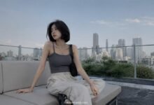 Acubi summer outfit with grey ribbed tank, cream cargo pants, black shoulder bag, black sandals, silver jewelry, and rooftop city styling