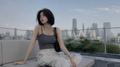 Acubi summer outfit with grey ribbed tank, cream cargo pants, black shoulder bag, black sandals, silver jewelry, and rooftop city styling