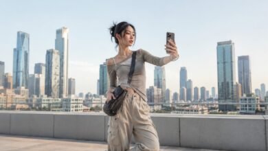 Woman taking a selfie in an Acubi outfit with asymmetrical grey top, beige cargo pants, crossbody bag, silver jewelry, and chunky sneakers