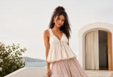 Woman wearing a cream babydoll top with a soft blush maxi skirt in a bright coastal setting