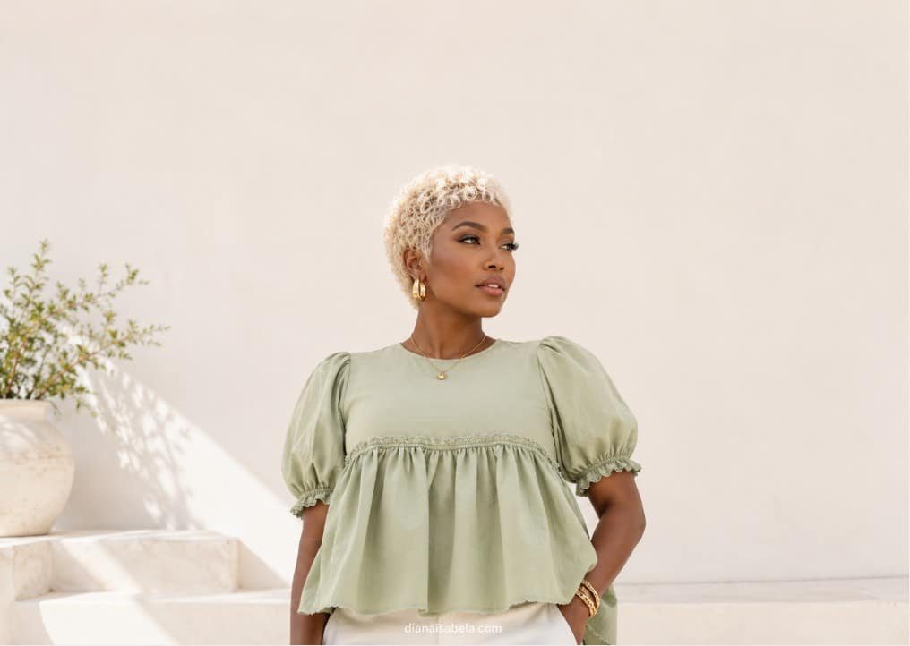 Woman with short blonde curls wearing a sage green babydoll top in a clean minimalist fashion portrait
