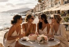 Stylish friends celebrating a birthday at a seaside café with cake, candles, flowers, and golden coastal light