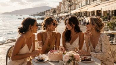 Stylish friends celebrating a birthday at a seaside café with cake, candles, flowers, and golden coastal light