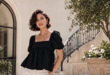 Woman wearing a black babydoll top with cream trousers in a clean elegant courtyard outfit