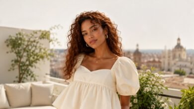 Woman with curly red hair wearing a cream babydoll top in a sunlit rooftop fashion setting