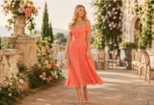 Blonde woman in a coral June wedding guest dress at a romantic summer garden reception
