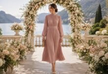 Modest wedding guest dress with long sleeves under a romantic floral wedding arch by the lake