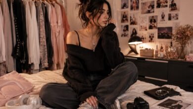 Fashion blogger sitting in a cozy bedroom closet with moodboard wall, clothing rack, oversized sweater, loose jeans, sneakers, headphones, camera, and accessories