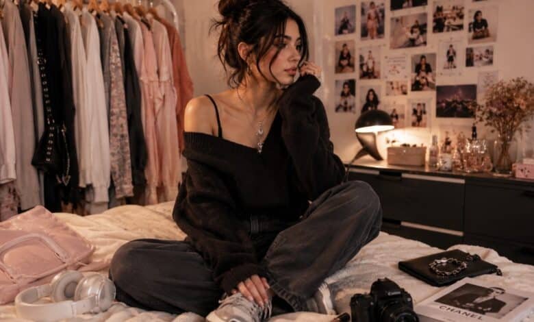 Fashion blogger sitting in a cozy bedroom closet with moodboard wall, clothing rack, oversized sweater, loose jeans, sneakers, headphones, camera, and accessories