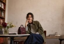 Stylish woman in an olive utility jacket, striped top and dark denim seated in an independent bookshop café for a fashion brand editorial