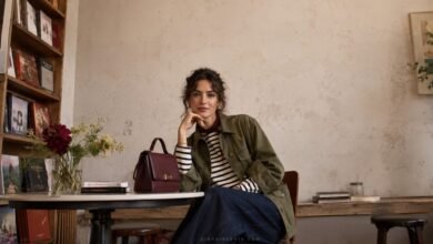 Stylish woman in an olive utility jacket, striped top and dark denim seated in an independent bookshop café for a fashion brand editorial