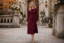 Woman in an elegant burgundy long-sleeve midi dress outside a decorated historic church for a fall wedding