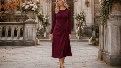 Woman in an elegant burgundy long-sleeve midi dress outside a decorated historic church for a fall wedding