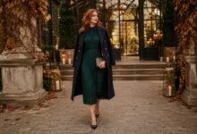 Fall wedding guest dress for cold weather in deep green styled with a tailored navy coat, black heels, and an evening clutch.