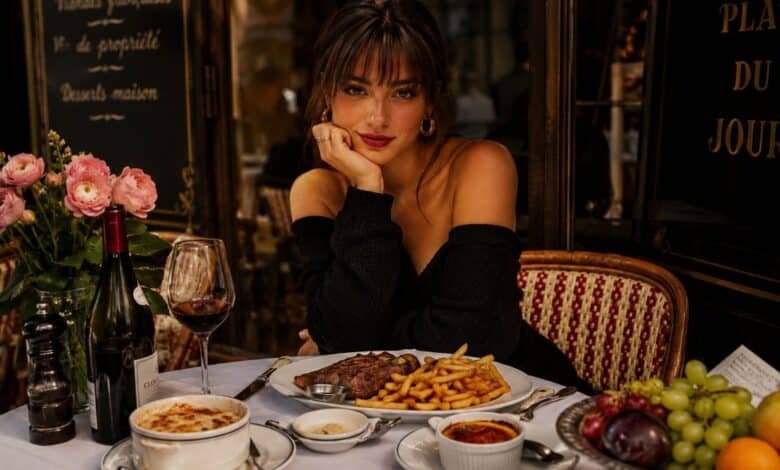 Stylish woman at a French bistro table with steak frites, onion soup, crème brûlée, wine, flowers, fruit and Paris restaurant mood