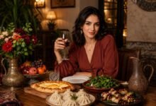 Stylish Georgian dinner table with khachapuri, khinkali, eggplant rolls, fresh herbs, fruit, flowers, and a woman enjoying wine in a warm restaurant setting.