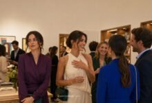 Two stylish friends at an art gallery opening, with one receiving attention while the other watches with a subtle, unreadable expression.